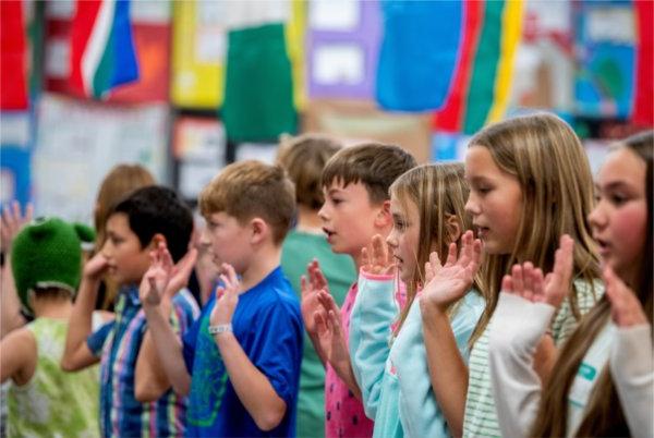  Middle-school aged children stand in a line with the palm of their hands facing out. 他们后面挂着许多彩旗和海报. 