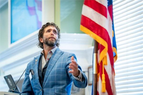 一个人 stands at a podium and looks up at an American flag that is standing near him.  