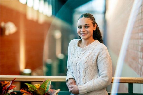 一个人 stands on an indoor balcony looking at the camera and smiling. 