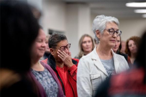  一个人 standing in a crowd indoors wipes a tear from their eye. 