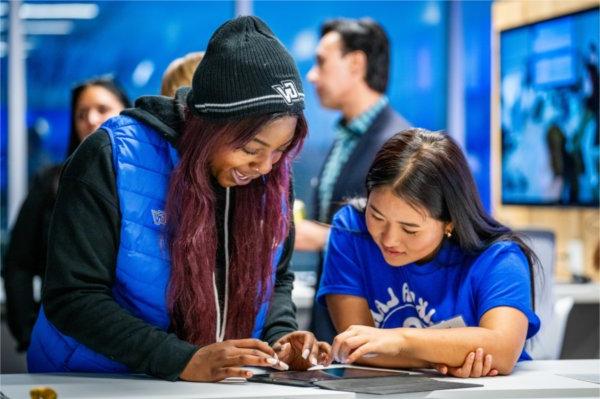 Two people stand close together at a high top table crouching over a tablet together. 