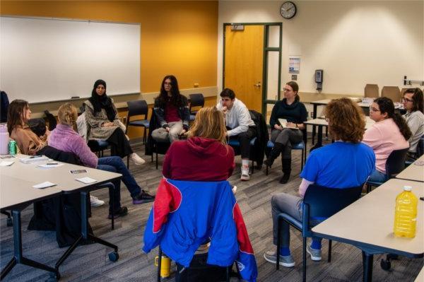 students sitting in chairs in a circle in a classroom, having a discussion