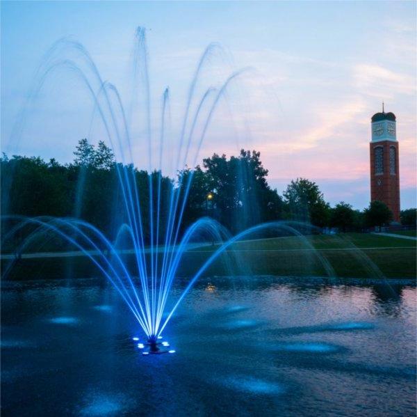 Zumberge Pond fountain lit in blue at twilight with carillon tower in background